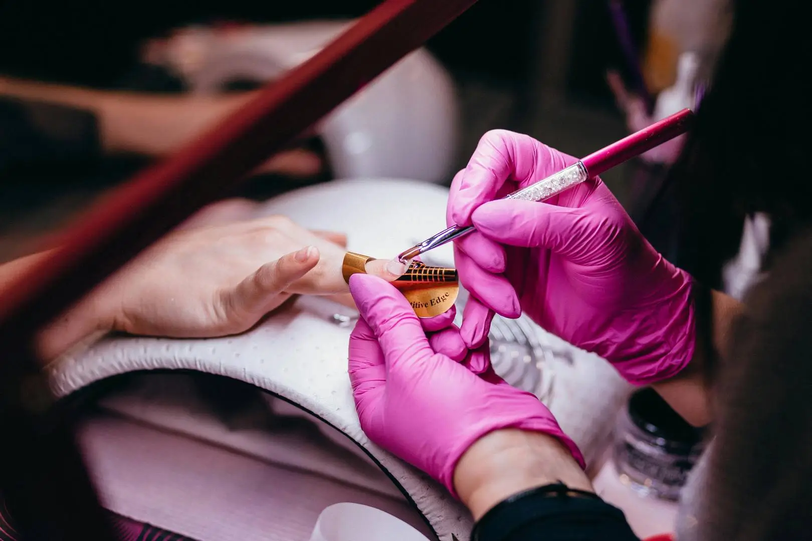 Zabieg stylizacji paznokci w gabinecie Beauty Place & School – stylistka w różowych rękawiczkach przedłuża paznokieć metodą żelową.