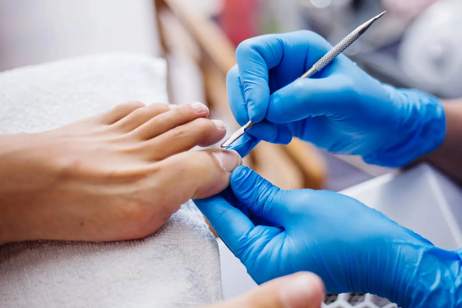 Zabieg podologiczny w gabinecie Beauty Place & School – specjalistyczna pielęgnacja paznokci stóp wykonywana przez osobę w niebieskich rękawiczkach.